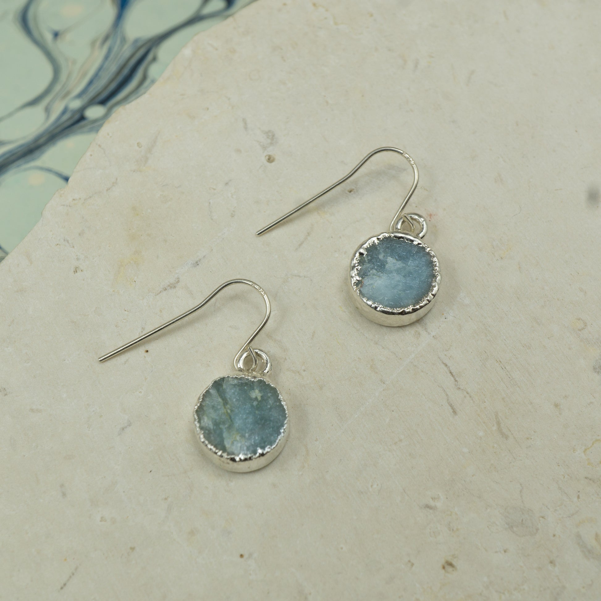 Round raw Blue aquamarine earrings on hooks finished in silver.
