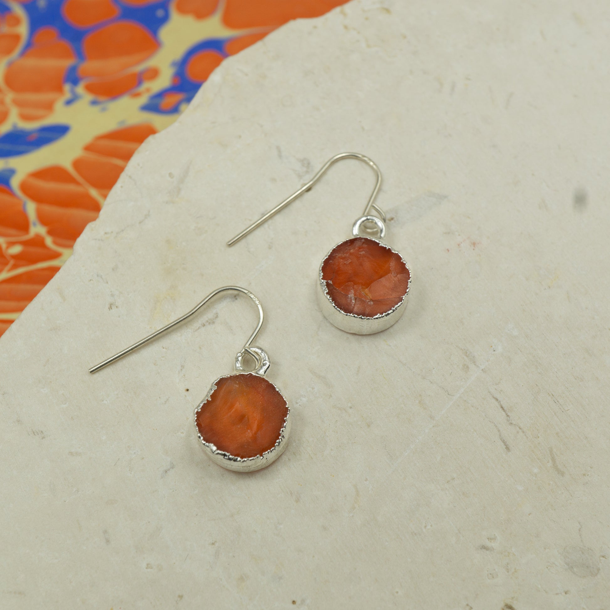 Round raw orange carnelian earrings on hooks finished in silver.