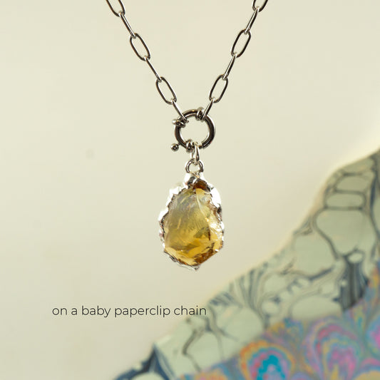 A silver paperclip chain necklace with a raw, irregular yellow citrine gemstone pendant.
