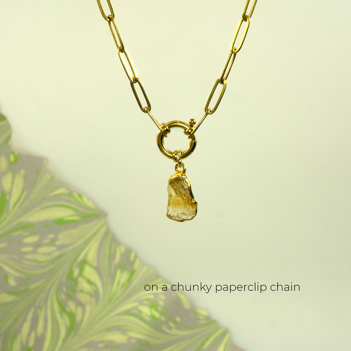 A gold paperclip chain necklace with a ring clasp and a raw, irregular amber-yellow stone citrine pendant