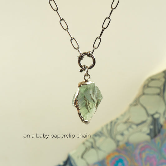 A silver paperclip chain necklace with a raw, irregular light Green Amethyst gemstone pendant