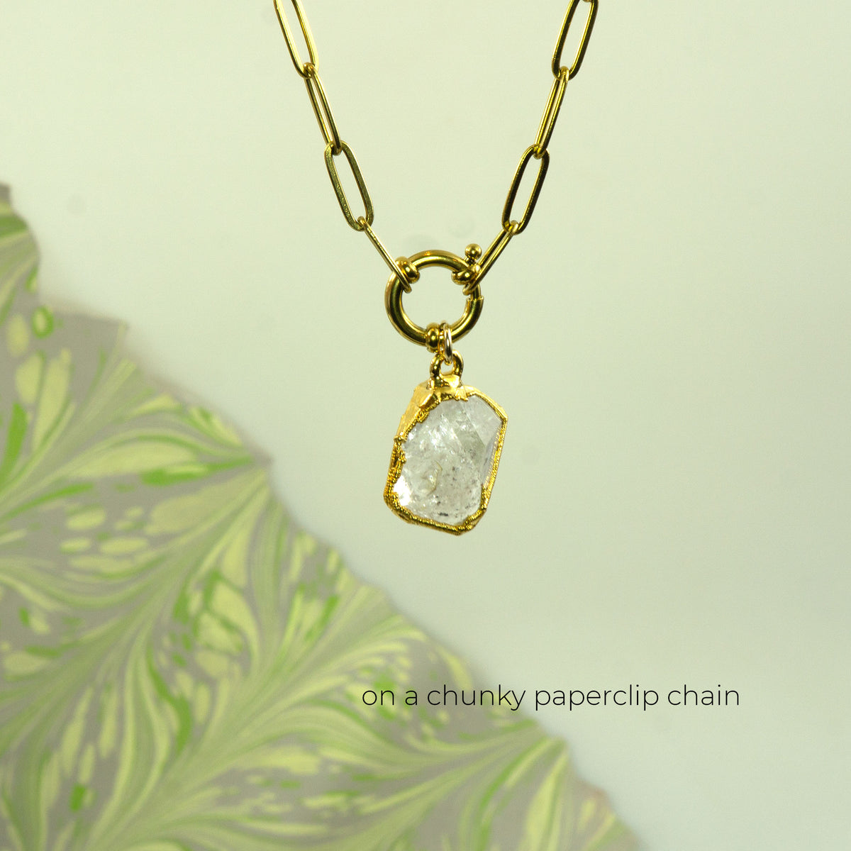 A gold necklace with a chunky paperclip chain and a raw, rough-cut clear raw Herkimer Diamond pendant