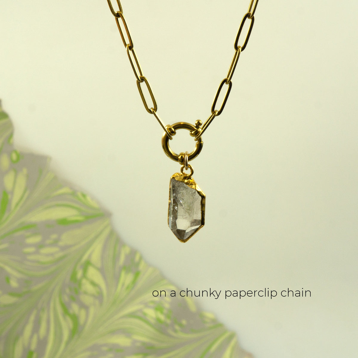 A gold-toned paperclip chain necklace with a clear faceted raw Herkimer Diamond pendant