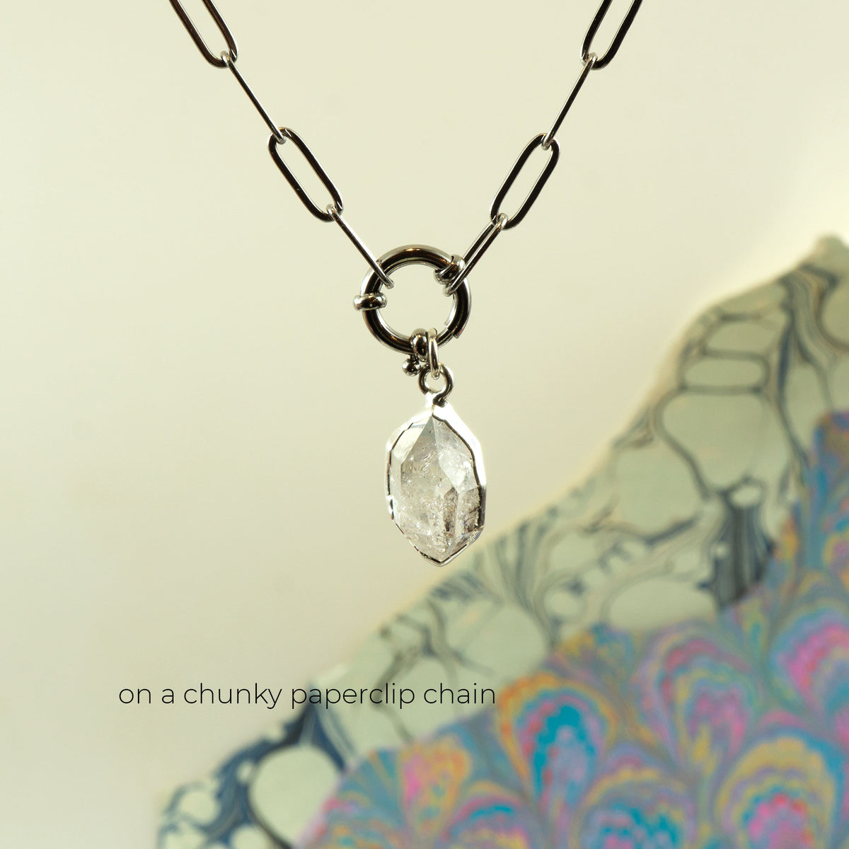 A silver paperclip chain necklace with a clear faceted gemstone pendant