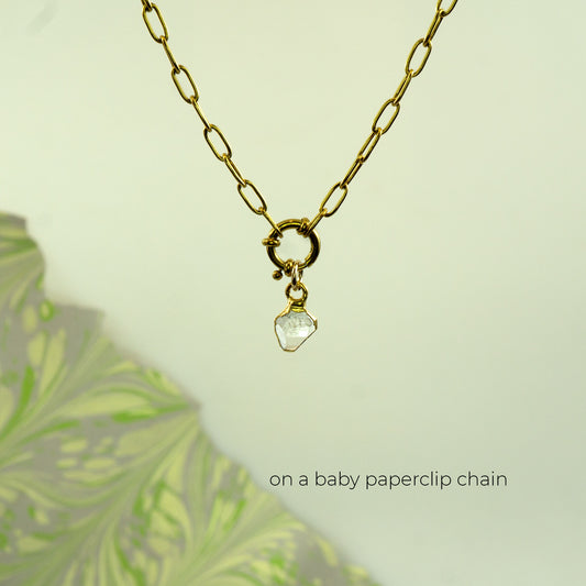 A gold paperclip chain necklace with a small gold clasp and a clear faceted herkimer diamond stone pendant