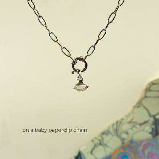 A silver paperclip chain necklace with a small ring clasp and a tiny faceted clear Herkimer Diamond gemstone pendant