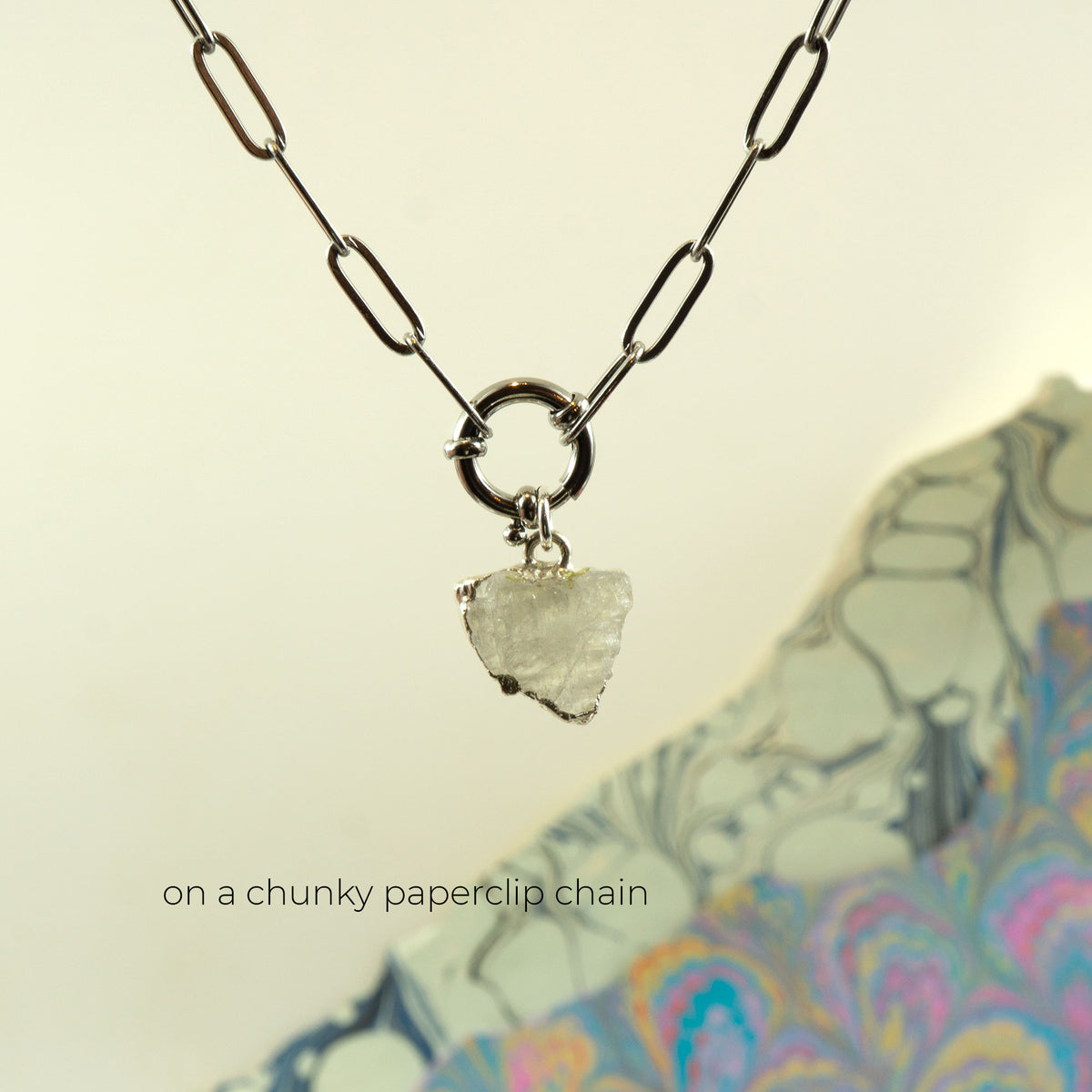 A silver paperclip chain necklace with a small triangular clear Rainbow Moonstone pendant