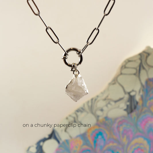 A silver paperclip chain necklace with a large ring connector and a raw, faceted clear Rainbow Moonstone crystal pendant.