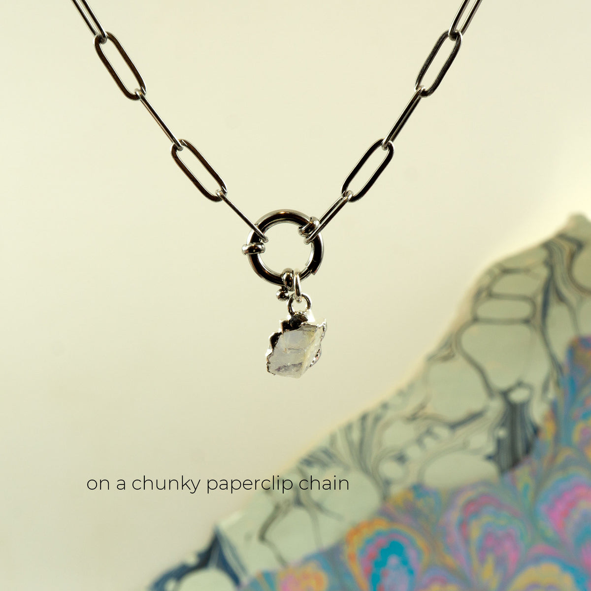 A silver paperclip chain necklace with a small clear faceted Rainbow Moonstone pendant