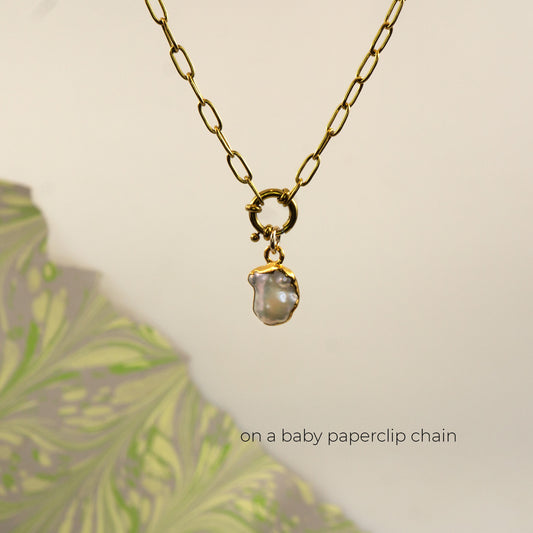A gold paperclip chain necklace with a small gold ring clasp holding an irregular, pearl pendant,