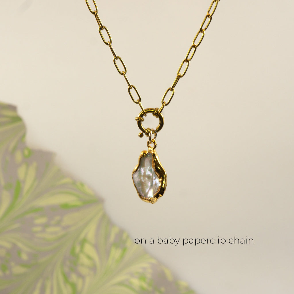 A gold paperclip chain necklace with a small gold ring clasp holding an irregular pearl pendant
