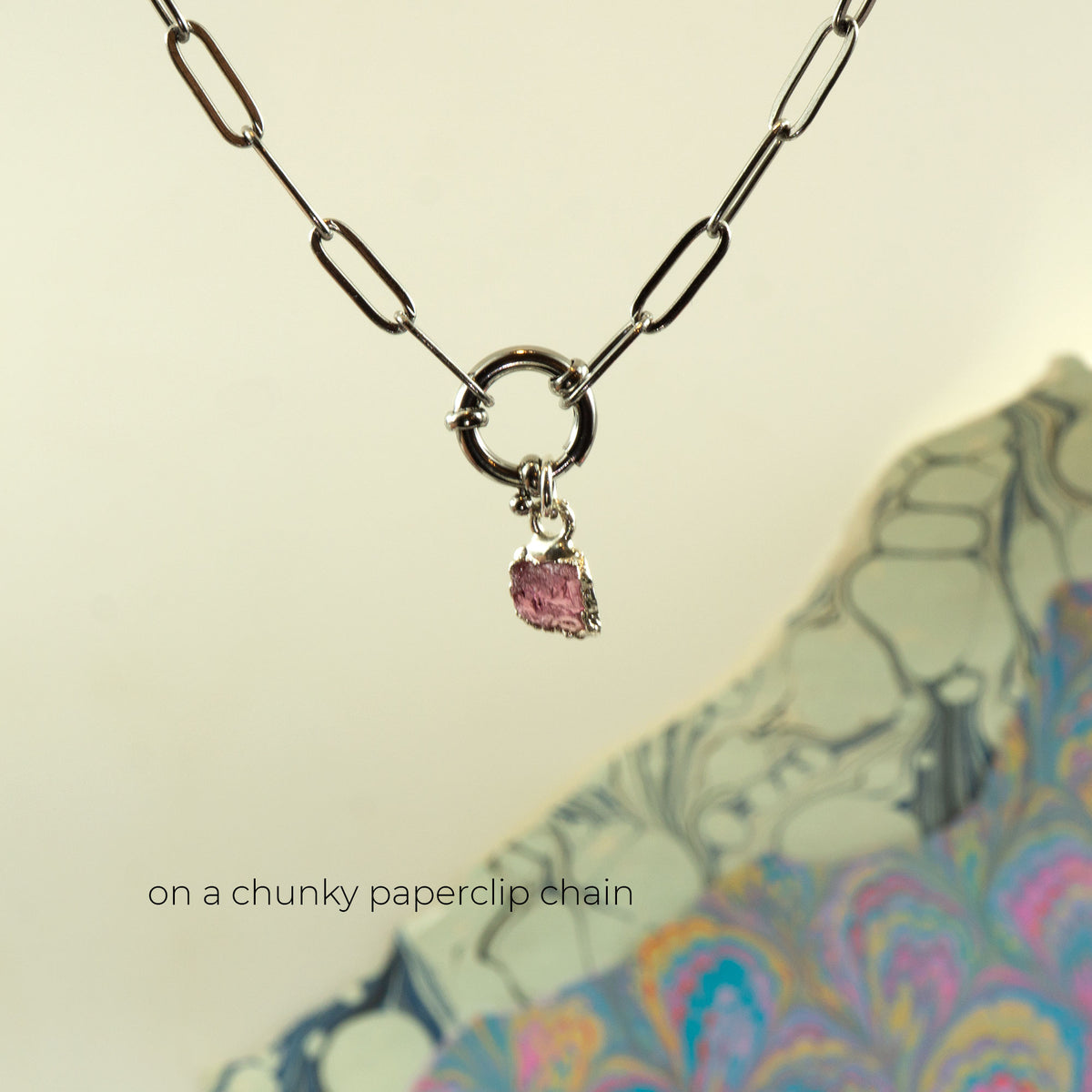 A silver paperclip chain necklace with a circular ring clasp and a small dangling Pink Tourmaline gemstone