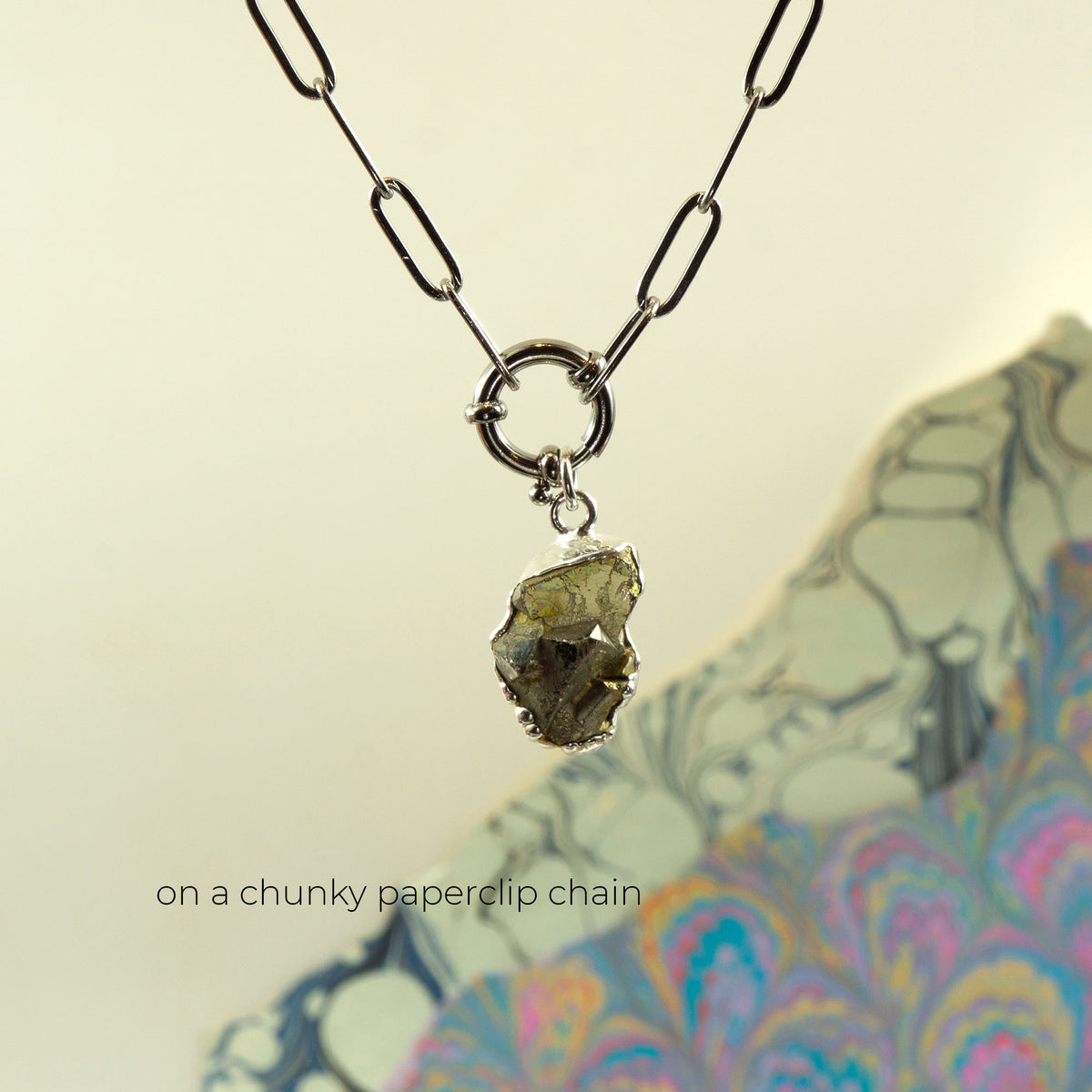 A necklace with a chunky silver paperclip chain and a raw, rough pyrite gemstone pendant