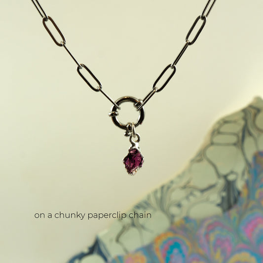 A silver paperclip chain necklace with a small ring clasp and a dangling faceted pink rhodolite garnet gemstone