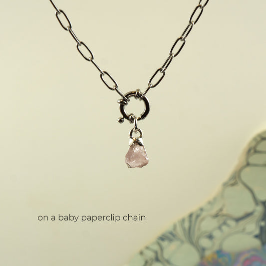 A silver paperclip chain necklace with a small silver ring clasp and a dangling raw pink rose quartz stone