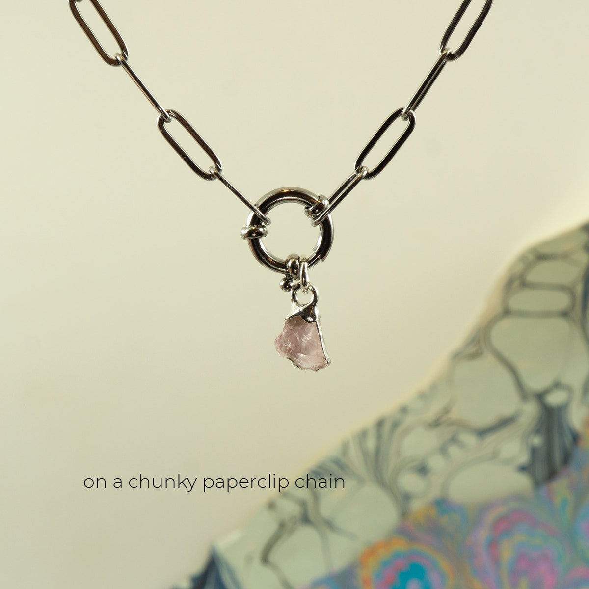 A silver paperclip chain necklace with a circular ring clasp and a small pink rose quartz stone charm