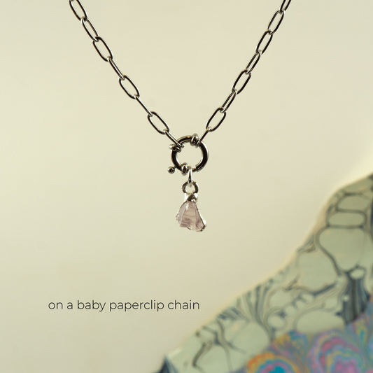 A silver paperclip chain necklace with a small silver ring clasp and a dangling light pink rose quartz stone charm