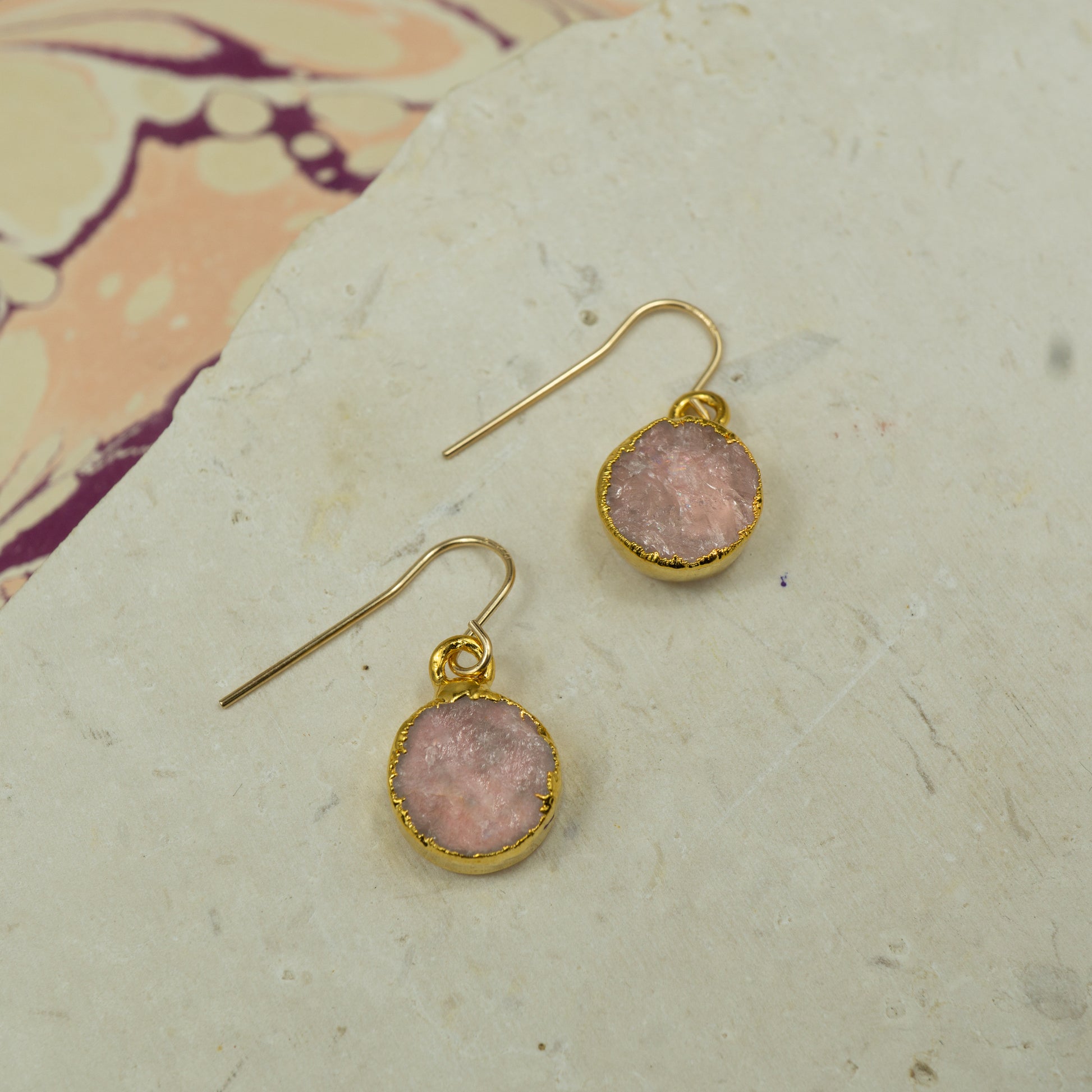 Round raw pink rose quartz earrings on hooks finished in gold.