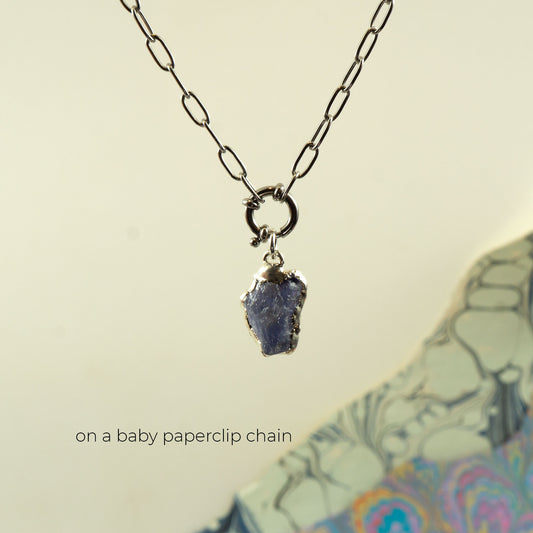 Blue-purple raw tanzanite gemstone pendant embezzled in solid silver, on a delicate plain silver paperclip chain.