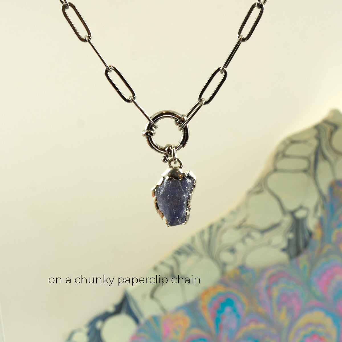 irregular shaped blue-purple raw tanzanite gemstone pendant embezzled in solid silver, on a chunky silver paperclip chain.