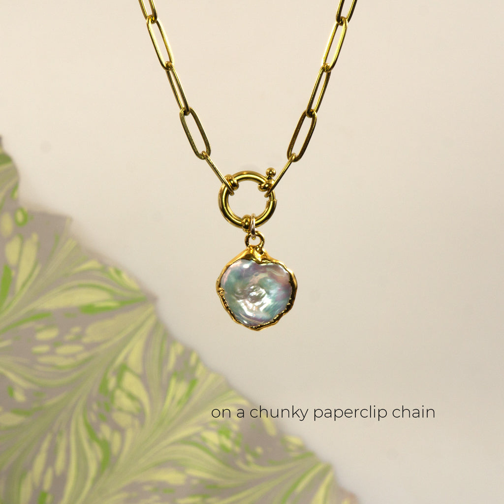 A gold paperclip chain necklace with a small round ring connector and an irregular iridescent pearl pendant