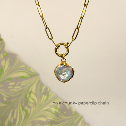 A gold paperclip chain necklace with a small round ring connector and an irregular iridescent pearl pendant