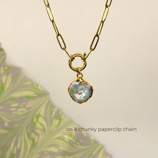 A gold paperclip chain necklace with a small round ring connector and an irregular iridescent pearl pendant
