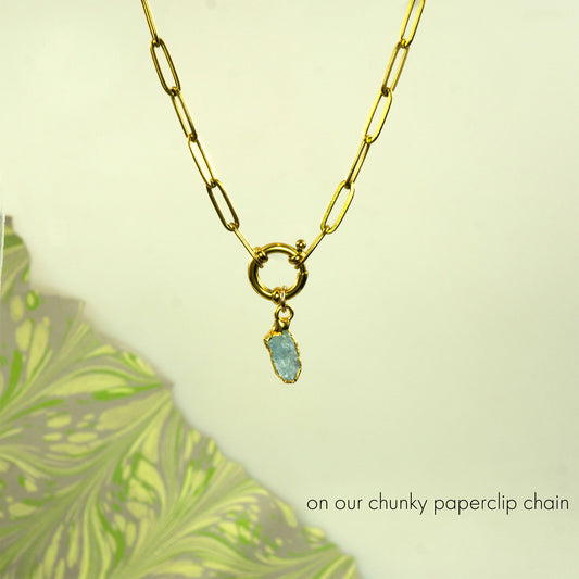 A gold paperclip chain necklace with a toggle clasp and a small light aquamarine gemstone pendant