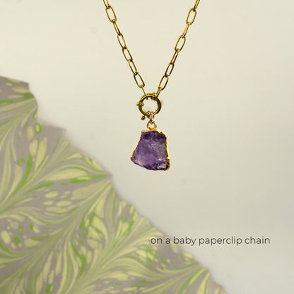 A gold paperclip chain necklace with a raw purple amethyst stone pendant set in a gold bezel 