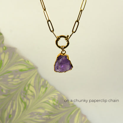 A gold paperclip chain necklace with a raw purple amethyst gemstone pendant set in gold