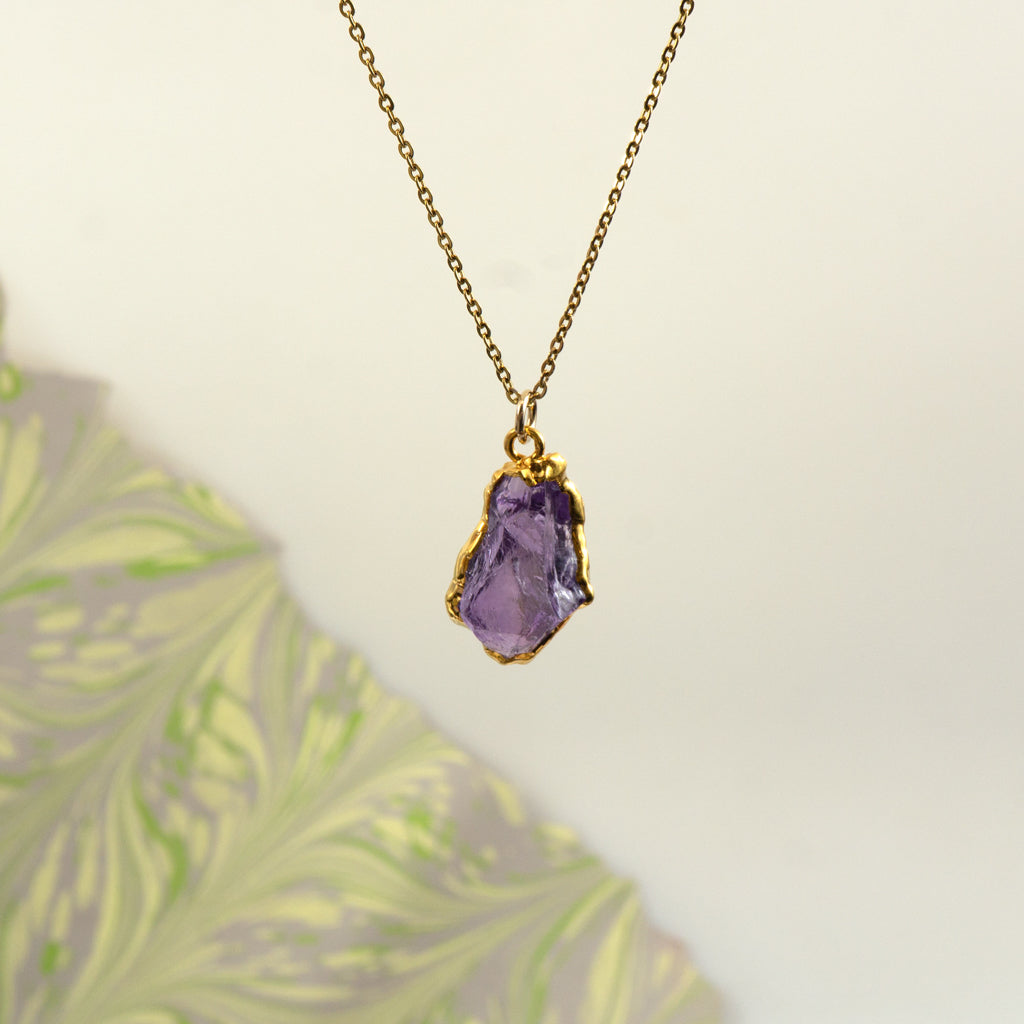 A gold chain necklace with a raw, Amethyst pendant,