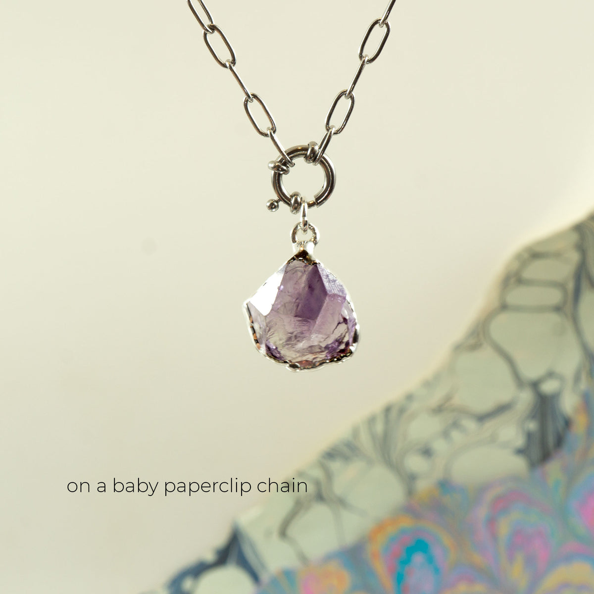 A silver baby paperclip chain necklace with a ring clasp and a faceted purple Amethyst gemstone pendant