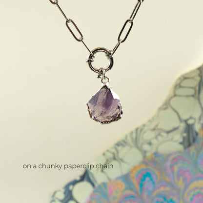 A silver chunky paperclip chain necklace with a ring clasp and a faceted purple Amethyst gemstone pendant