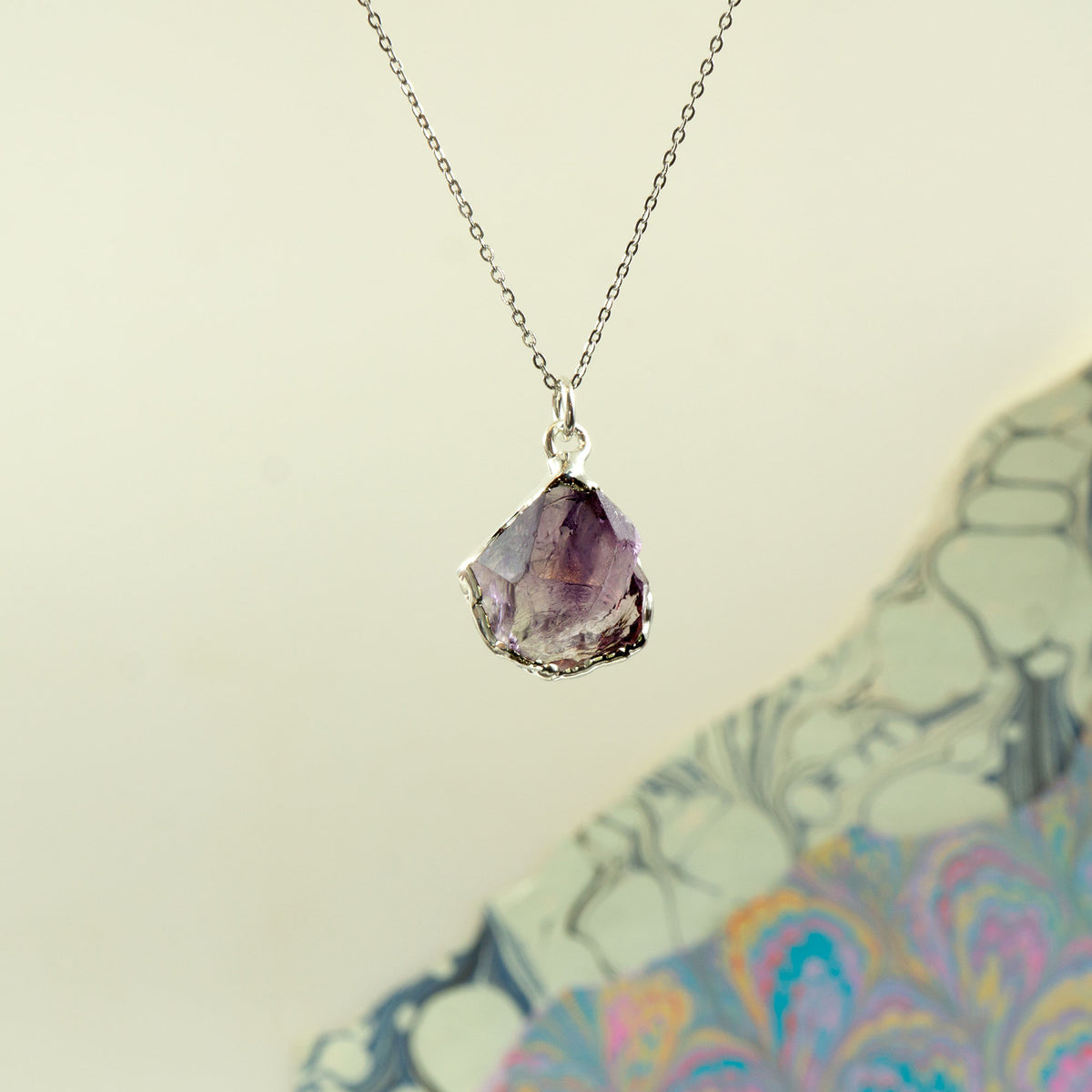 A silver chain necklace with a ring clasp and a faceted purple Amethyst gemstone pendant