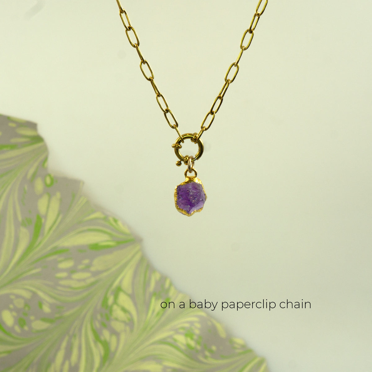 A gold paperclip chain necklace with a small gold ring clasp holding a raw  Amethyst purple gemstone pendant