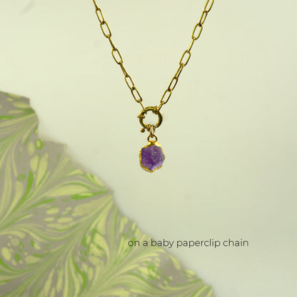 A gold paperclip chain necklace with a small gold ring clasp holding a raw  Amethyst purple gemstone pendant