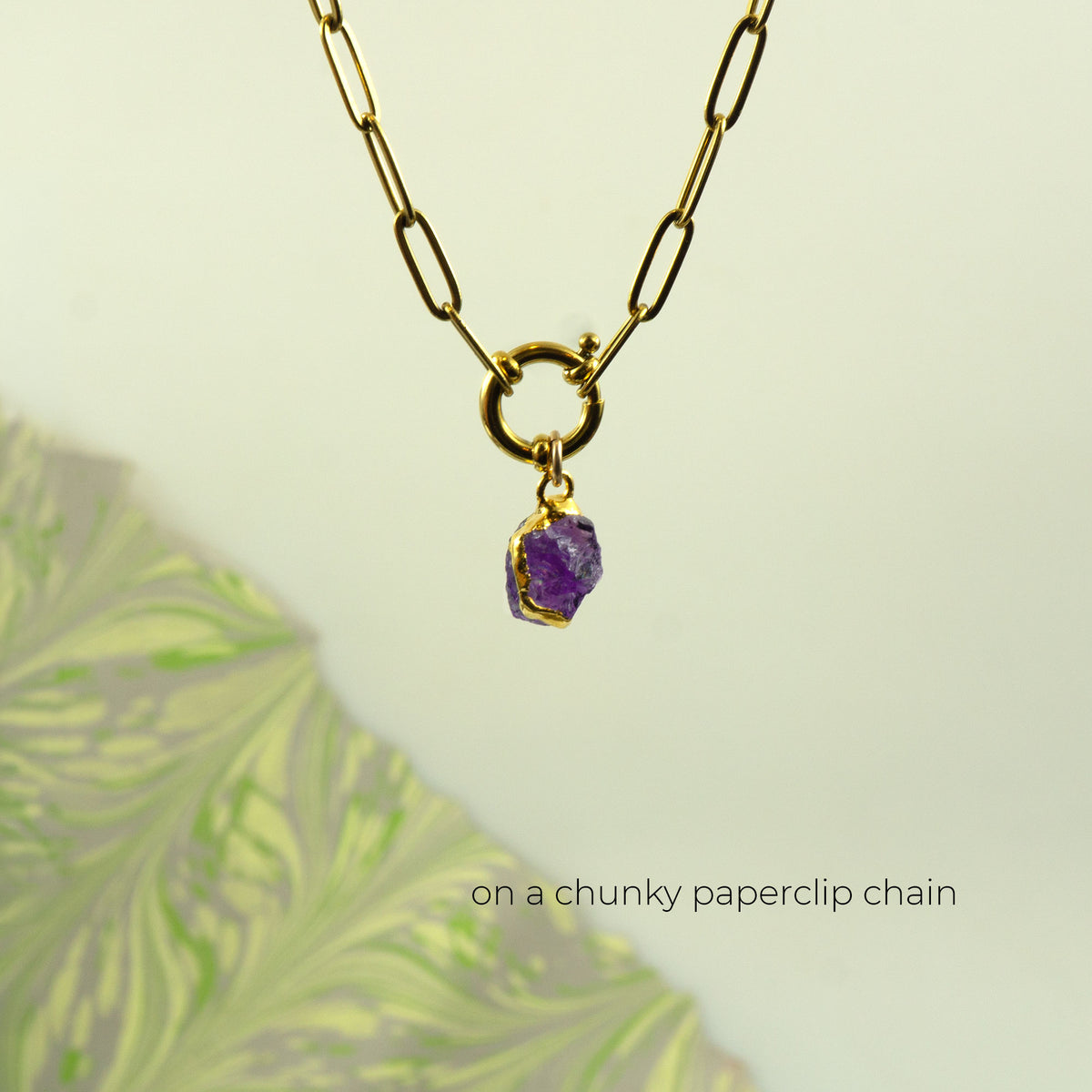 A gold chunky paperclip chain necklace with a ring clasp holding a raw Amethyst pendant.