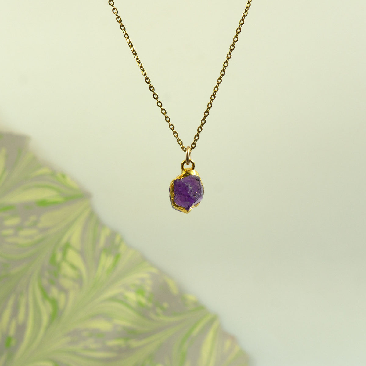 A gold paperclip chain necklace with a ring clasp holding a raw Amethyst pendant.