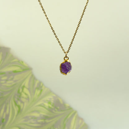 A gold paperclip chain necklace with a ring clasp holding a raw Amethyst pendant.