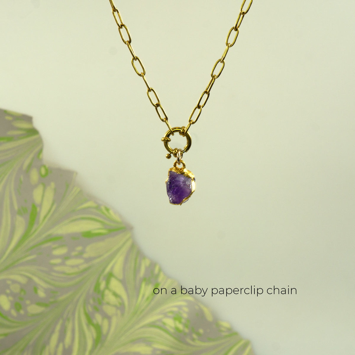 A gold paperclip chain necklace with a small gold ring clasp holding a raw purple amethyst pendant