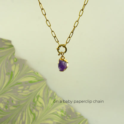 A gold paperclip chain necklace with a small gold ring clasp holding a raw purple amethyst pendant
