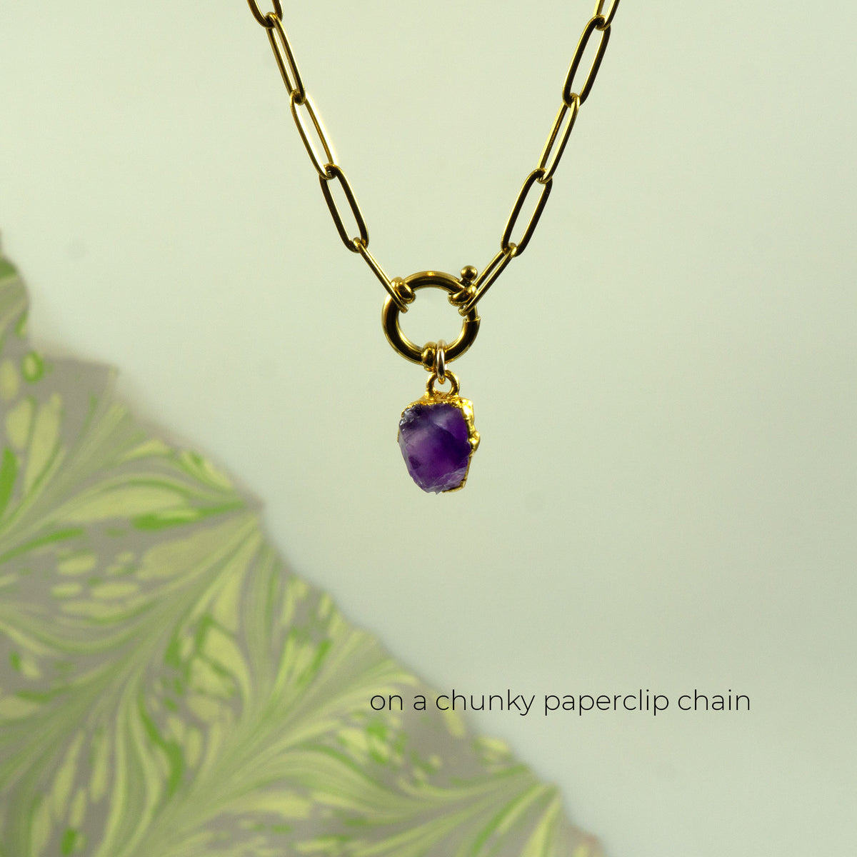 A gold chunky paperclip chain necklace with a small gold ring clasp holding a raw purple Amethyst stone pendant