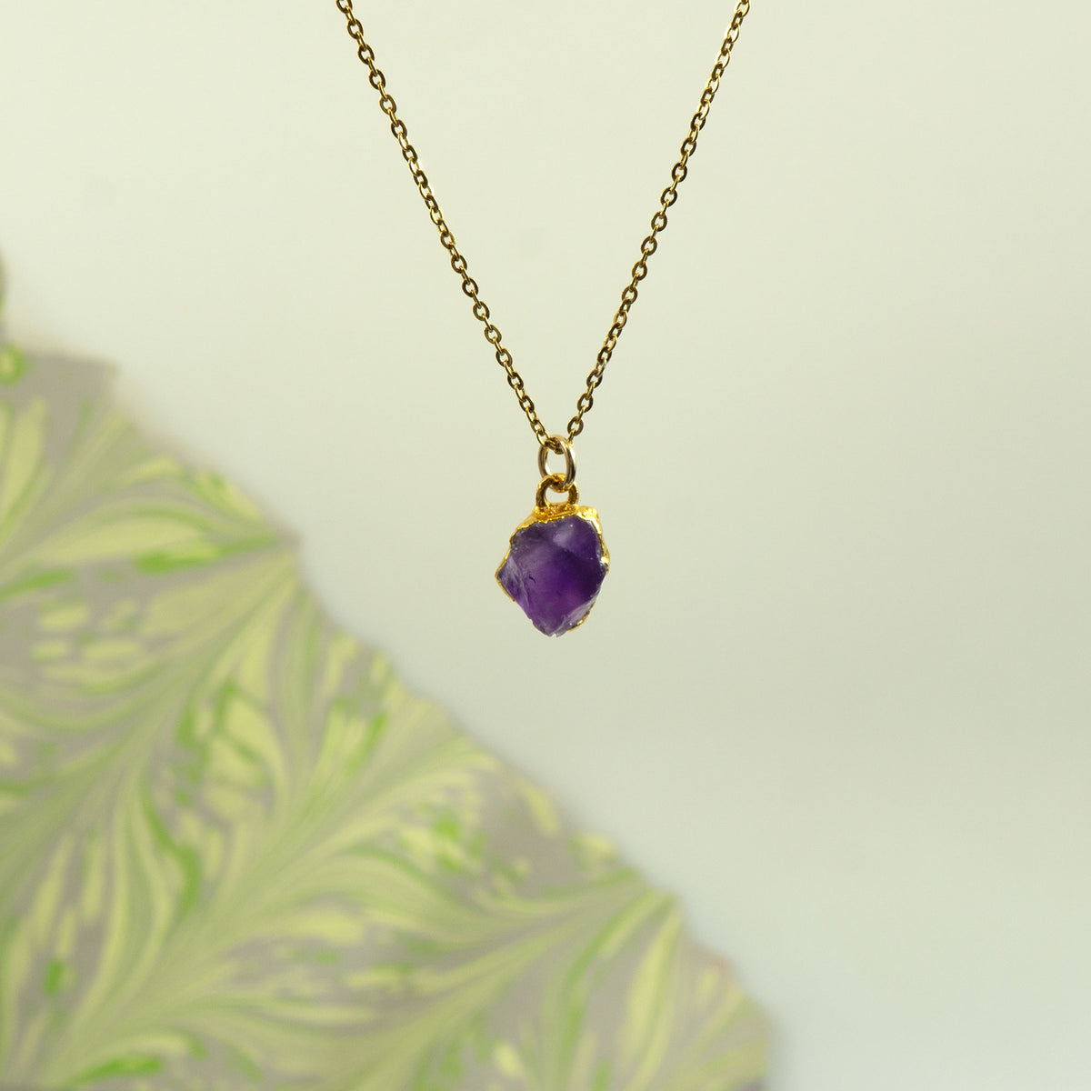A gold chain necklace with a small bezel-set purple stone pendant