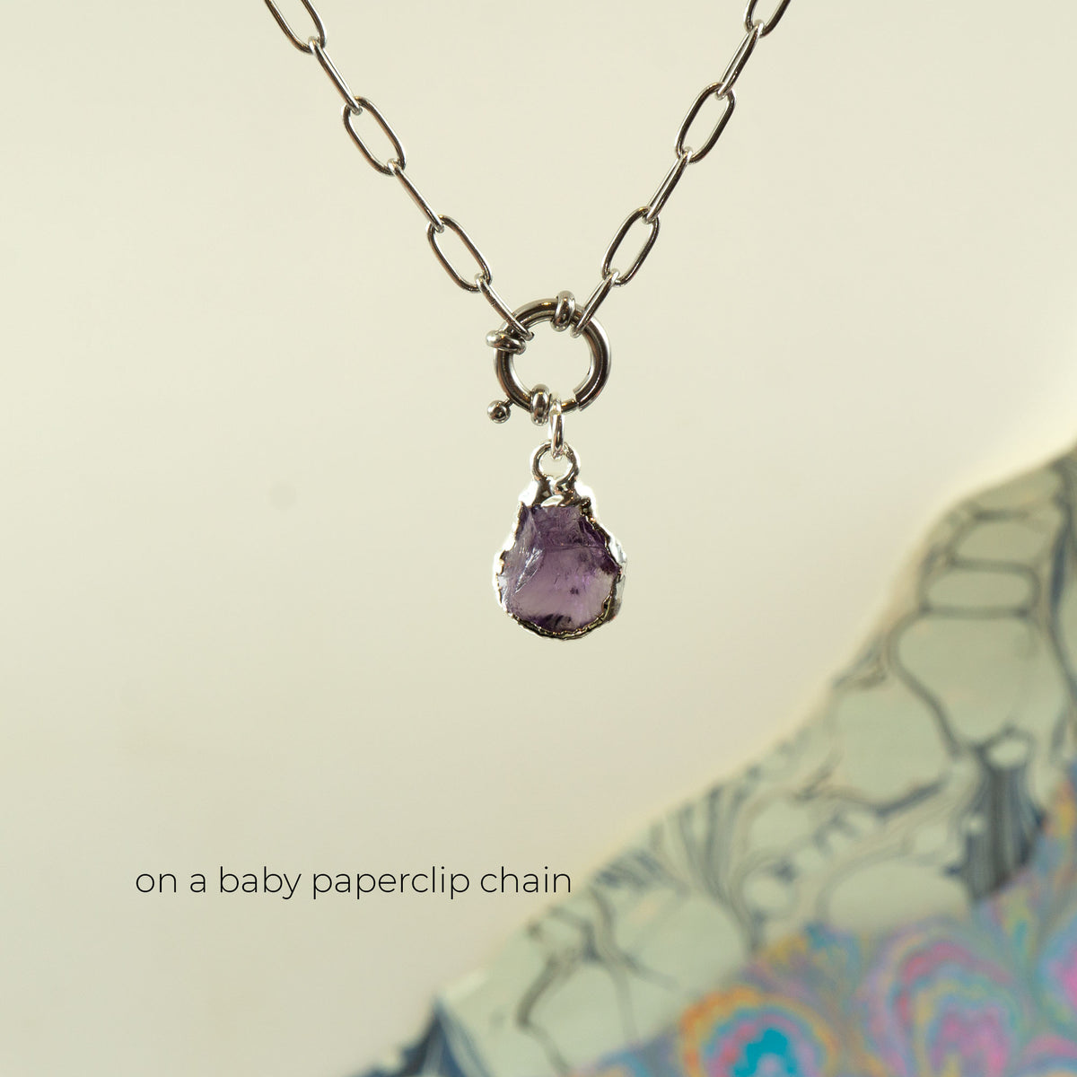 A silver chunky paperclip chain necklace with a small ring clasp holding a teardrop-shaped purple Amethyst gemstone pendant.