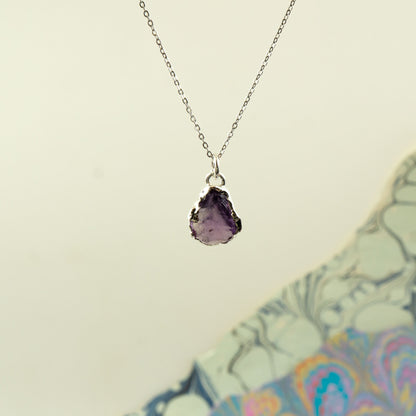 A silver chain necklace with a teardrop-shaped purple amethyst geode pendant.