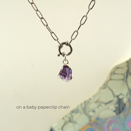 A silver baby paperclip chain necklace with a ring clasp and a small rough-cut Amethyst purple gemstone pendant.