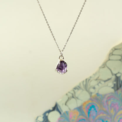 A silver chain necklace with a small, irregular-cut purple Amethyst gemstone pendant.