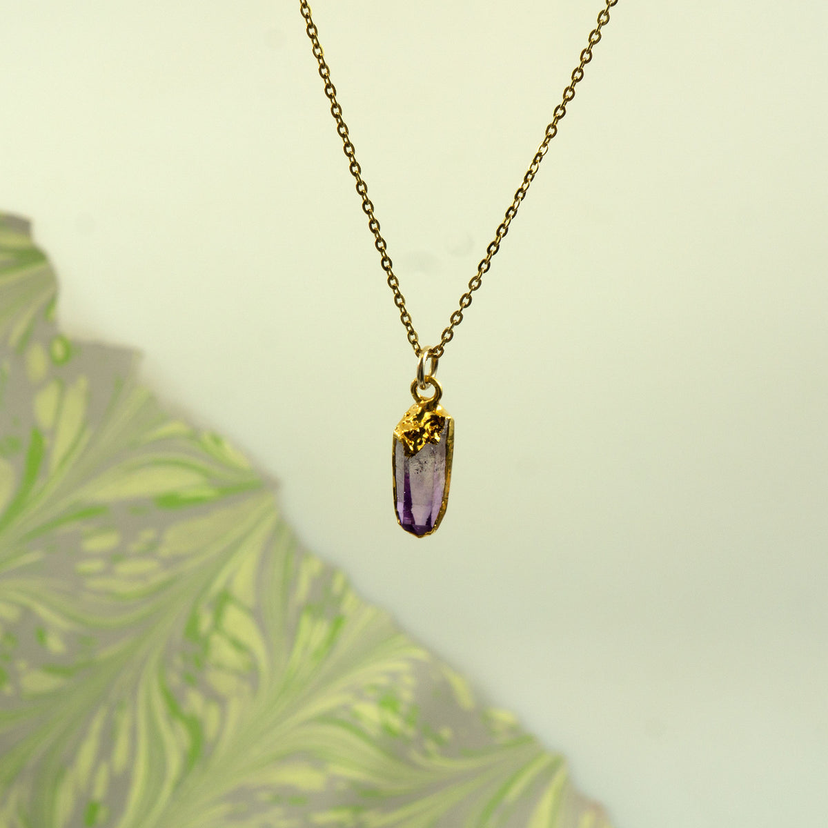 A gold chain necklace with a raw, unpolished purple amethyst crystal pendant