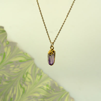 A gold chain necklace with a raw, unpolished purple amethyst crystal pendant