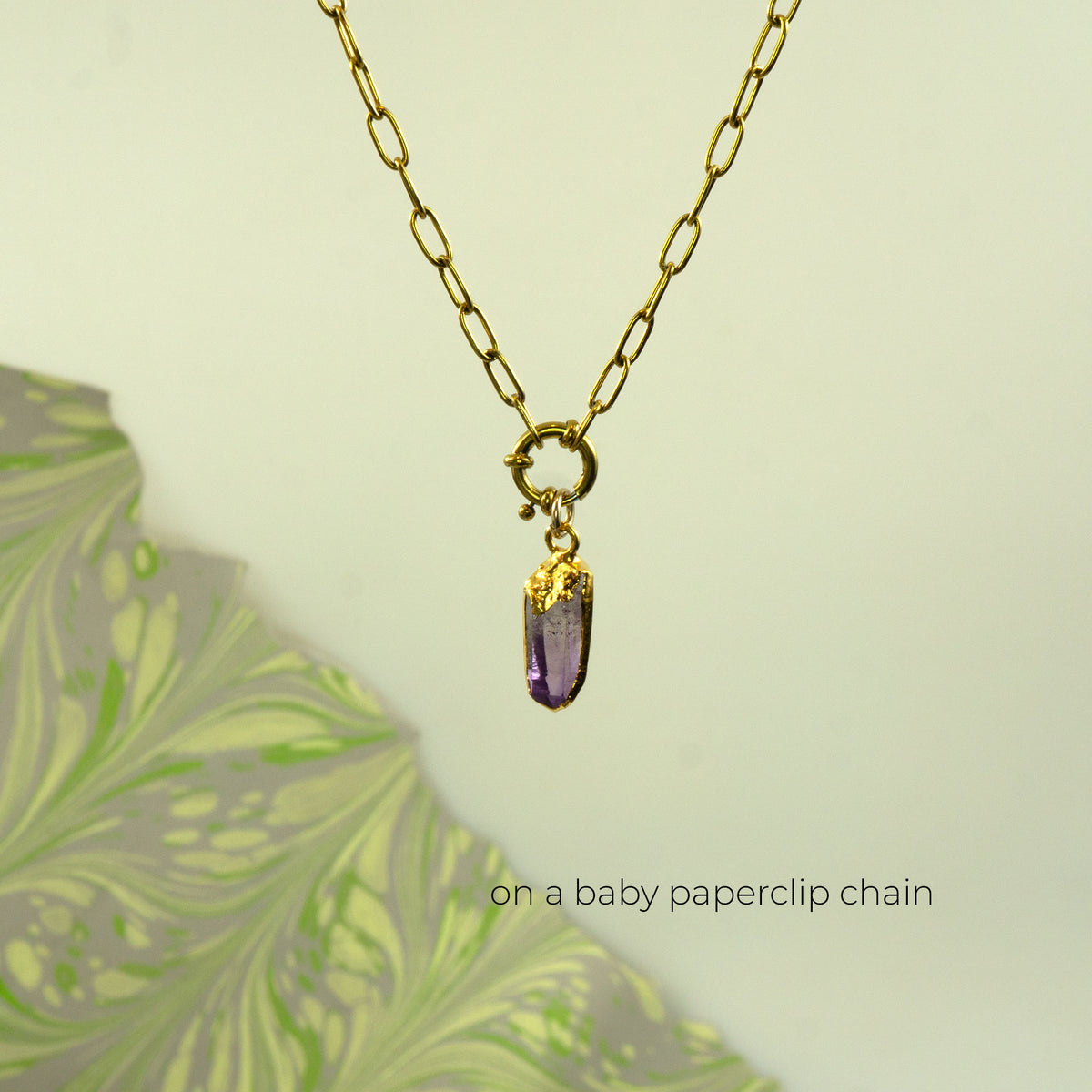 A gold paperclip chain necklace with a small gold ring clasp holding a polished purple crystal pendant
